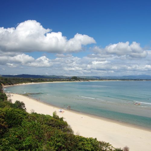Byron Bay, New South Wales, Australia  - October 29, 2016: Rainforest backs Clarkes Beach where people enjoy the sea off Clarkes Beach. Main Beach and the Byron Bay town centre are located at the centre of the photo.